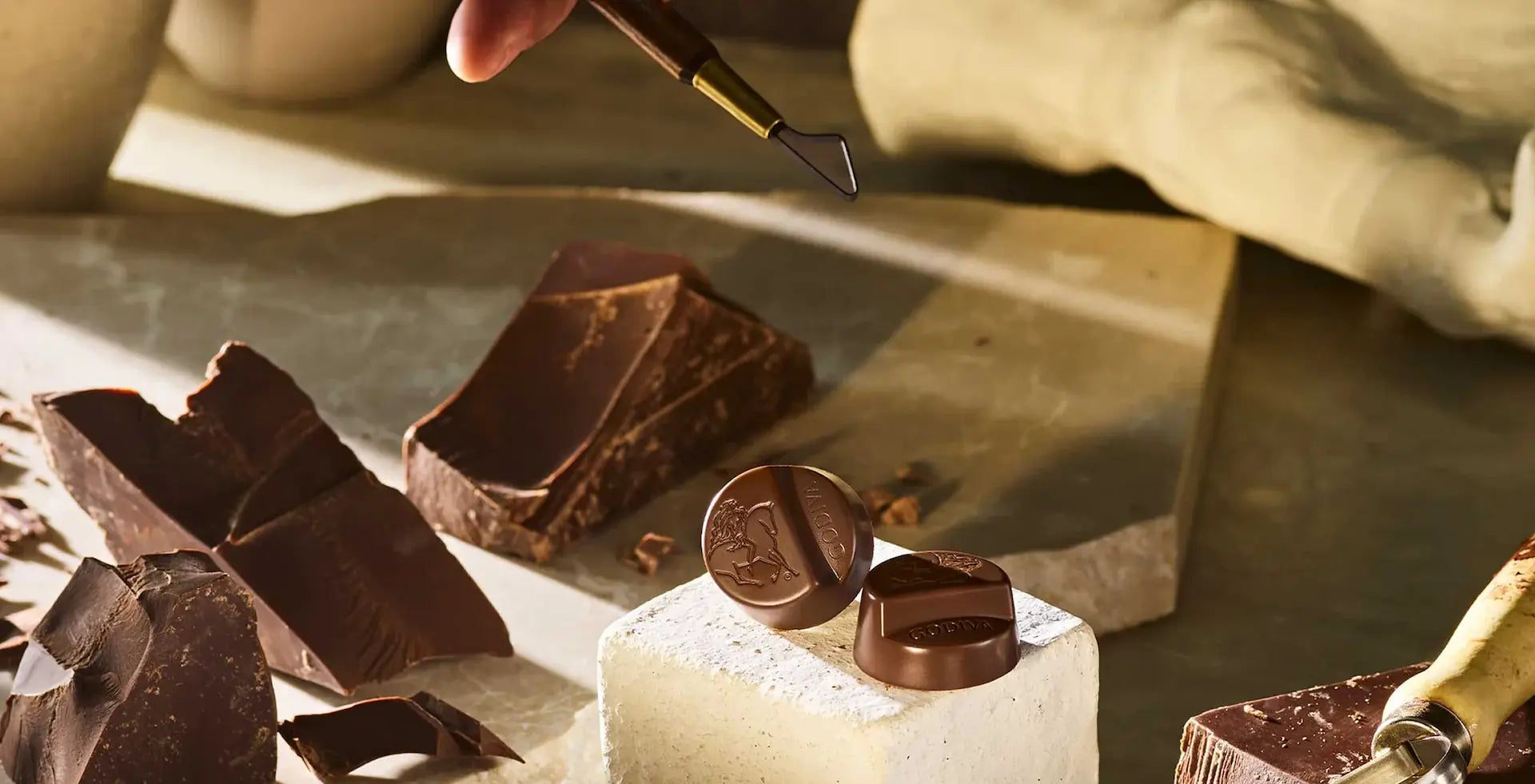 Hand using a tool to shape chocolate on a wooden surface