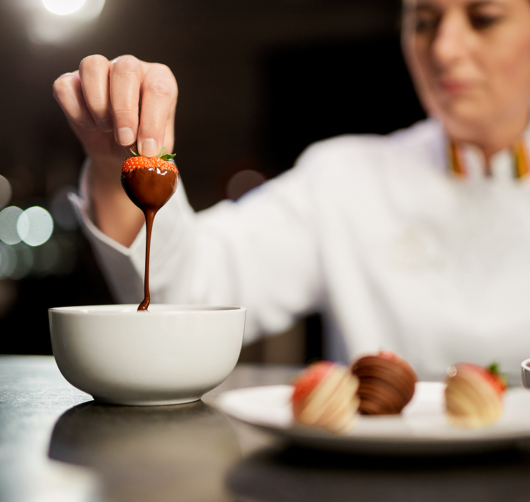 Chef dipping a strawberry into a bowl of chocolate sauce.