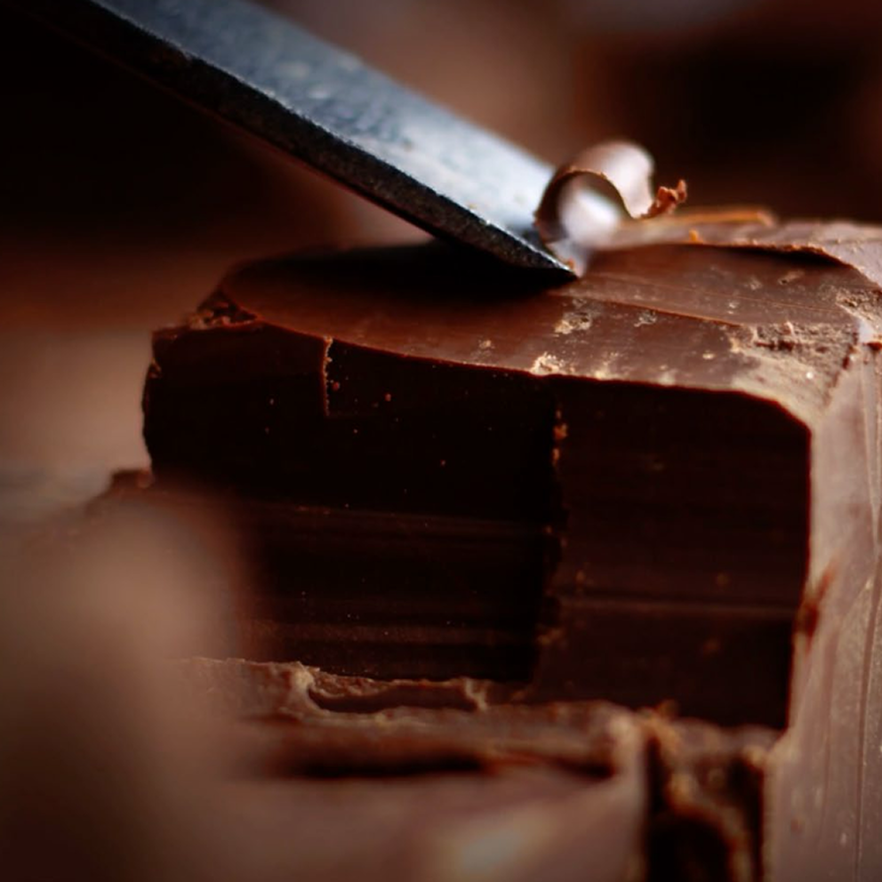 Close-up of a knife cutting through a block of dark chocolate.