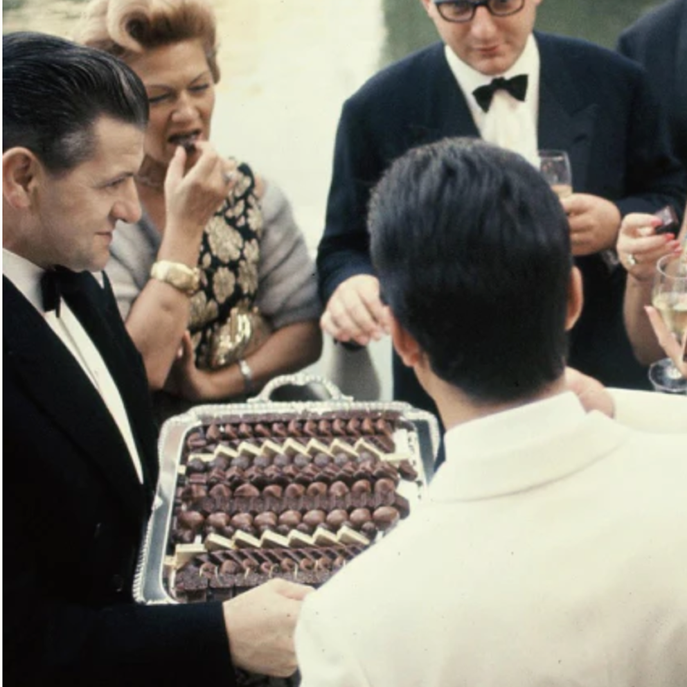 Vintage scene with a man serving chocolates at a formal event.