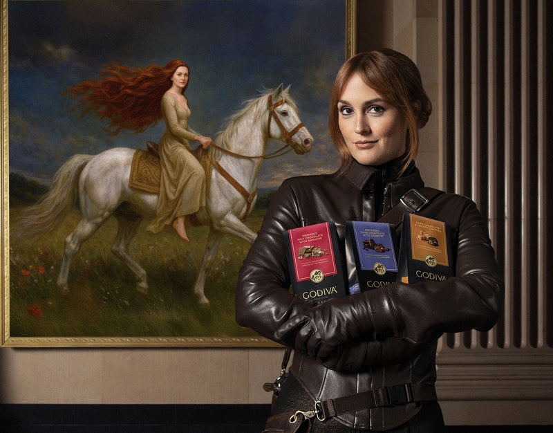 Person holding Godiva chocolate boxes in front of a painting of a woman on a horse